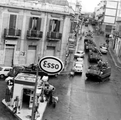 Colonna di mezzi blindati in una via del centro, accanto a un distributore Esso